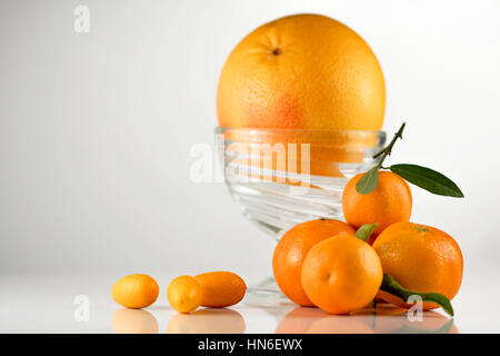 Orange juteuse dans un bol en verre placé sur un whitbackground avec quelques mandarines Banque D'Images