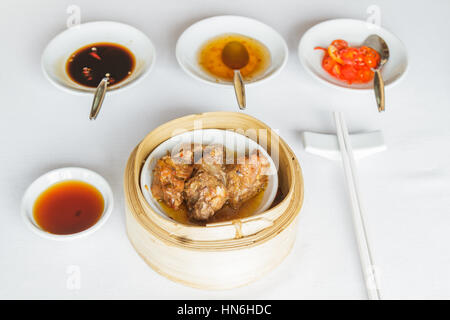Dim sum à la vapeur des aliments de côtes de porc en noir en panier de bambou au restaurant avec de la sauce soja, la sauce sucrée, sauce chili et baguettes. Banque D'Images