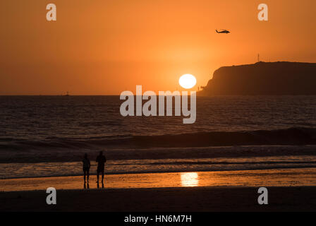 Couple watching orange et jaune spectaculaire coucher de soleil sur l'île de Coronado à San Diego en Californie avec l'hélicoptère Banque D'Images