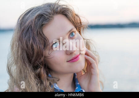 Jeune femme pensant, looking up and smiling en touchant le visage avec la main Banque D'Images