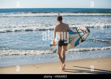 Avec les lignes de l'homme maillot de surf et marche sur la rive pour les vagues de l'océan Banque D'Images