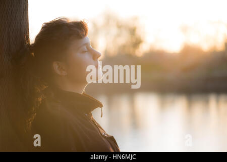 Portrait of young woman in nirvana pacifique coat aux yeux clos par le lac avec soft brown lumière d'automne Banque D'Images