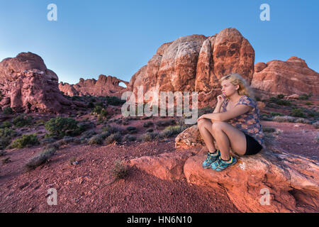 Young blonde woman sitting on rock en face de la skyline arch dans le parc national au crépuscule Banque D'Images