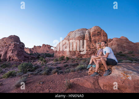 Young couple sitting on rock en face de skyline arch dans le parc national au crépuscule Banque D'Images