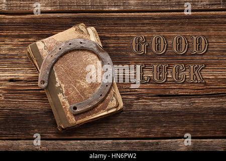 Old rusty horseshoe et livre sur fond de bois avec bonne chance inscription Banque D'Images