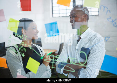 Des collègues en interaction les uns avec les autres lors de l'écriture sur sticky note in office Banque D'Images