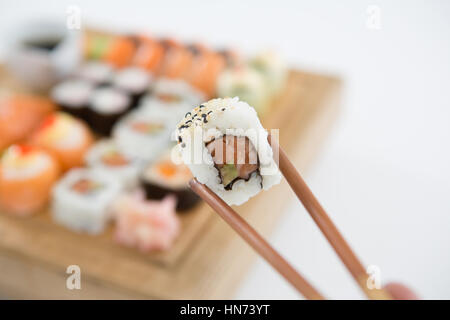 Close-up of sushi uramaki détenus dans des baguettes en bois Banque D'Images