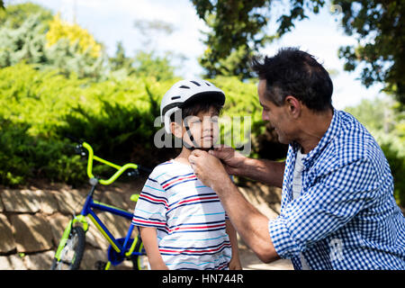 Père Fils aidant à porter un casque de vélo en stationnement sur une journée ensoleillée Banque D'Images