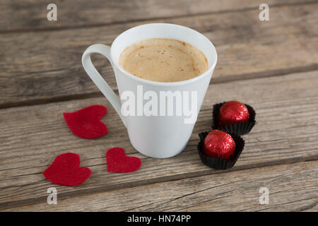 Tasse de café avec des chocolats en forme de coeur rouge et des pétales de rose sur la surface en bois Banque D'Images