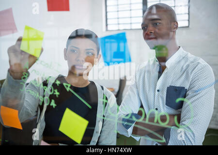 Des collègues de la lecture des notes autocollantes sur verre in office Banque D'Images