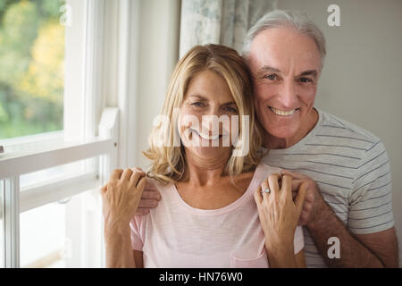 Portrait of happy senior couple standing next à la fenêtre à la maison Banque D'Images