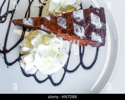 Cuisine italienne locale. Une tranche napolitaine typique italienne de Caprese Gâteau de chocolat et les amandes avec le chocolat fondu et fouetté crea Banque D'Images