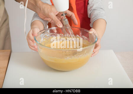 Trois ans enfant et femme mains crème à fouetter dans un bol en verre avec le mélangeur électrique, travail en équipe et de faire cuire un gâteau mousseline Banque D'Images