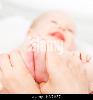 Gros plan sur trois mois baby girl recevoir massage des pieds d'une femme massothérapeute. La caméra est centrée sur les pieds de l'enfant. Heureux visage est flou Banque D'Images