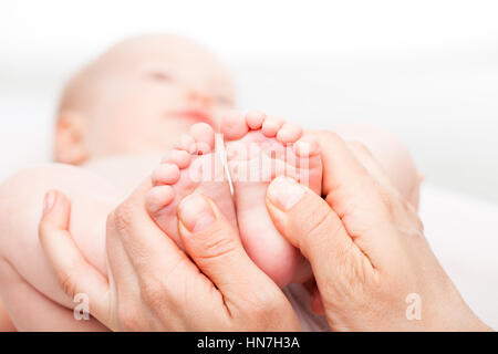 Gros plan sur trois mois baby girl recevoir massage des pieds d'une femme massothérapeute. La caméra est centrée sur les pieds de l'enfant. Visage est flou dans Banque D'Images