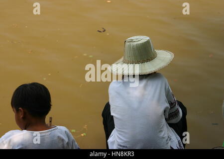 Deux hommes assis par un lac d'eau de couleur boueuse au Cambodge Banque D'Images