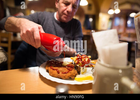 Senior man in restaurant met du ketchup sur les frites et schnitzel Banque D'Images
