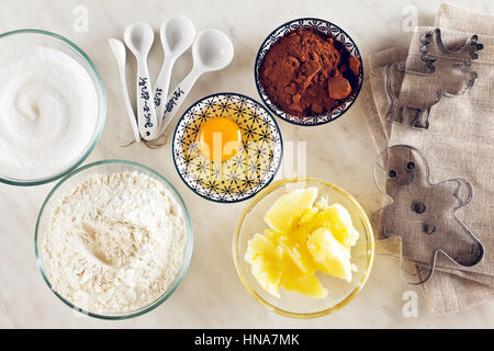 Ingrédients pour la cuisson sur une table de marbre blanc : farine, œufs, poudre de cacao, sucre, beurre et cuillères à mesurer, moules Banque D'Images