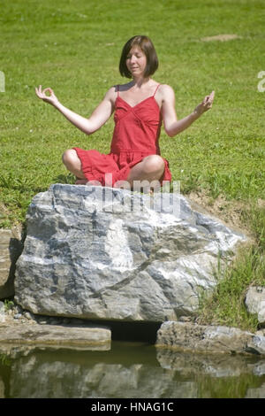 Junge Frau macht auf einem Jogauebungen Felsen am Teich - femme n'yoga Banque D'Images