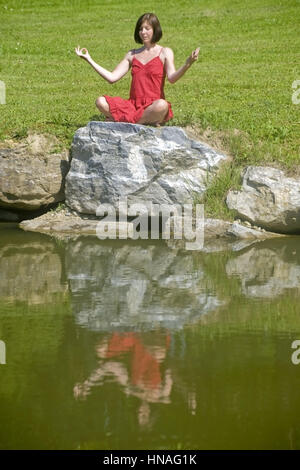 Junge Frau macht auf einem Jogauebungen Felsen am Teich - femme n'yoga Banque D'Images