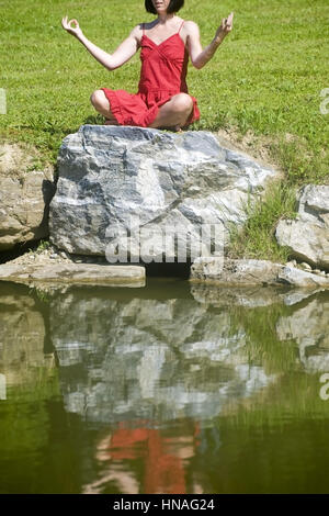 Junge Frau macht auf einem Jogauebungen Felsen am Teich - femme n'yoga Banque D'Images