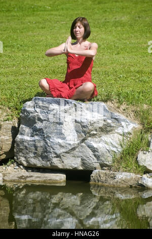 Junge Frau macht auf einem Jogauebungen Felsen am Teich - femme n'yoga Banque D'Images