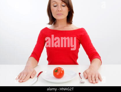 Junge Frau sitzt vor einem Teller mit einer Tomate darauf - Femme avec plaque à la tomate Banque D'Images