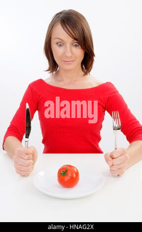 Junge Frau sitzt vor einem Teller mit einer Tomate darauf - Femme avec plaque à la tomate Banque D'Images