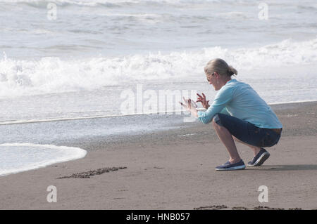 Femme à l'aide d'un téléphone cellulaire pour prendre une photo sur la plage. Banque D'Images