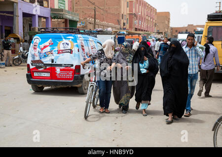 Marrakech, Maroc. Scène de rue, Marche des femmes voilées, jeune homme à l'aide de téléphone cellulaire. Banque D'Images