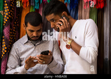 Marrakech, Maroc. Marché, deux jeunes hommes l'utilisation de téléphones cellulaires. Banque D'Images