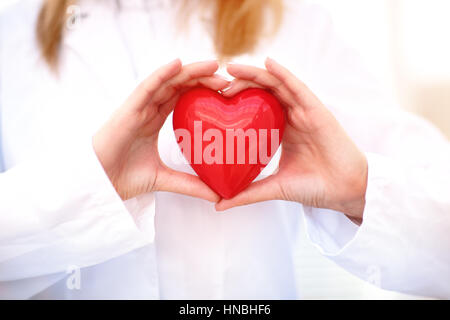 Jeune femme médecin tenant un cœur rouge, debout sur fond gris Banque D'Images