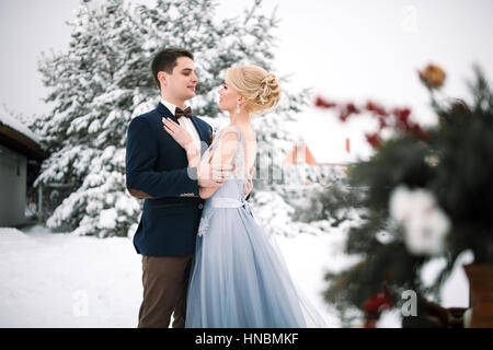 Mariage d'hiver en plein air sur fond de sapins couverts de neige. Mariée et le marié sont debout et s'étreindre. Ce qui est visible d'un grand sapin. Banque D'Images