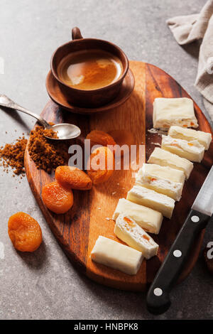 Tranches de Turrón sur une planche en bois avec des abricots secs, figues séchées et une tasse de café. collation santé, super aliment Banque D'Images