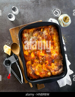 Lasagne aux italienne classique avec des légumes et le vin rouge dans le plat de cuisson sur un fond noir en gris, parmesan renversé .rosemary, vieille cuillère . Voir Banque D'Images