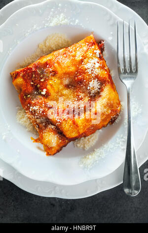 Lasagne au fromage entre les feuilles en couches de pâtes italiennes traditionnelles servi sur une plaque blanche sur un comptoir de bar ou restaurant sombre Banque D'Images