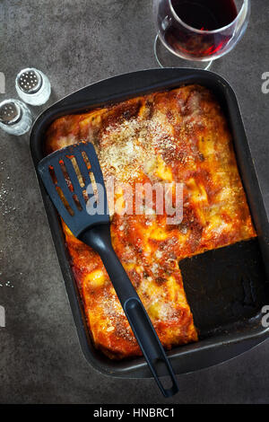 Lasagne aux italienne classique avec des légumes et le vin rouge dans le plat de cuisson sur un fond noir en gris, parmesan renversé .rosemary, vieille cuillère . Voir Banque D'Images