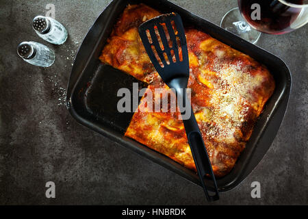 Lasagne aux italienne classique avec des légumes et le vin rouge dans le plat de cuisson sur un fond noir en gris, parmesan renversé .rosemary, vieille cuillère . Voir Banque D'Images