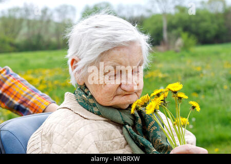 Photo d'une vieille femme tenant une fleur jaune Banque D'Images