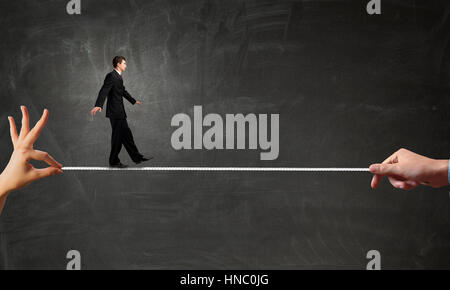 Attention businessman walking sur la corde dans les mains tendues Banque D'Images