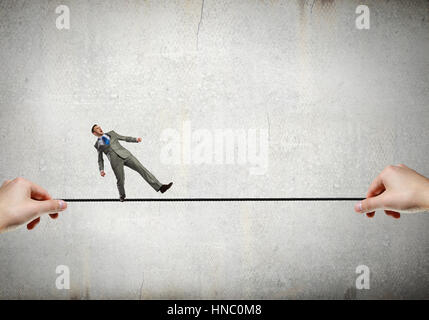 Attention businessman walking sur la corde dans les mains tendues Banque D'Images