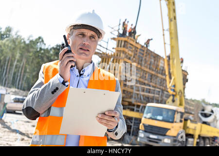 Superviseur en utilisant talkie walkie en maintenant le presse-papiers at construction site Banque D'Images