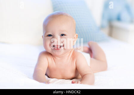 Bébé garçon vêtu de blanc à couches chambre ensoleillée. Le nouveau-né de se détendre dans le lit. Garderie pour les enfants. Literie et textile pour les enfants. Matin à la famille h Banque D'Images