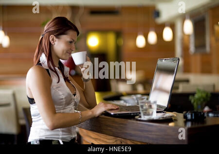 Communiqué de modèle, Junge Frau sitzt im Kaffeehaus an der Theke und arbeitet suis coffre - young woman using laptop in cafeteria Banque D'Images