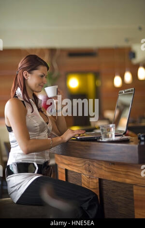 Communiqué de modèle, Junge Frau sitzt im Kaffeehaus an der Theke und arbeitet suis coffre - young woman using laptop in cafeteria Banque D'Images