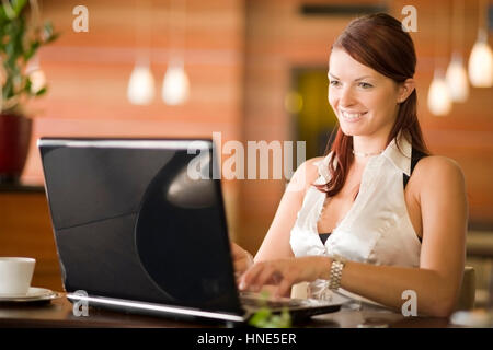 Communiqué de modèle, Junge Frau sitzt im Kaffeehaus an der Theke und arbeitet suis coffre - young woman using laptop in cafeteria Banque D'Images