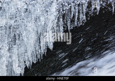 Glaçons suspendus au-dessus de l'eau congelée streaming de cascade en hiver Banque D'Images