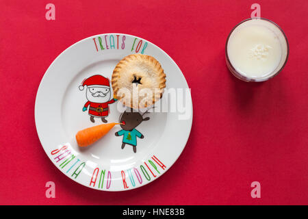 M&S de Noël toutes les butter mince pie à la carotte sur Noël fête assiette et le verre de lait comme gâteries pour le Père Noël et Rudolf isolé sur fond rouge Banque D'Images