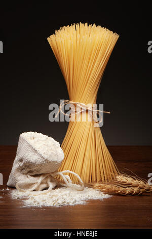 Les pâtes spaghetti sec attaché avec une corde de jute, sac de farine et les épis de blé sur la table en bois sombre sur fond gris Banque D'Images