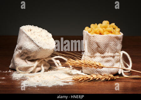 Sacs de jute de farine et pâtes cavatappi à sec, les épis de blé sur la table en bois sombre sur fond gris Banque D'Images